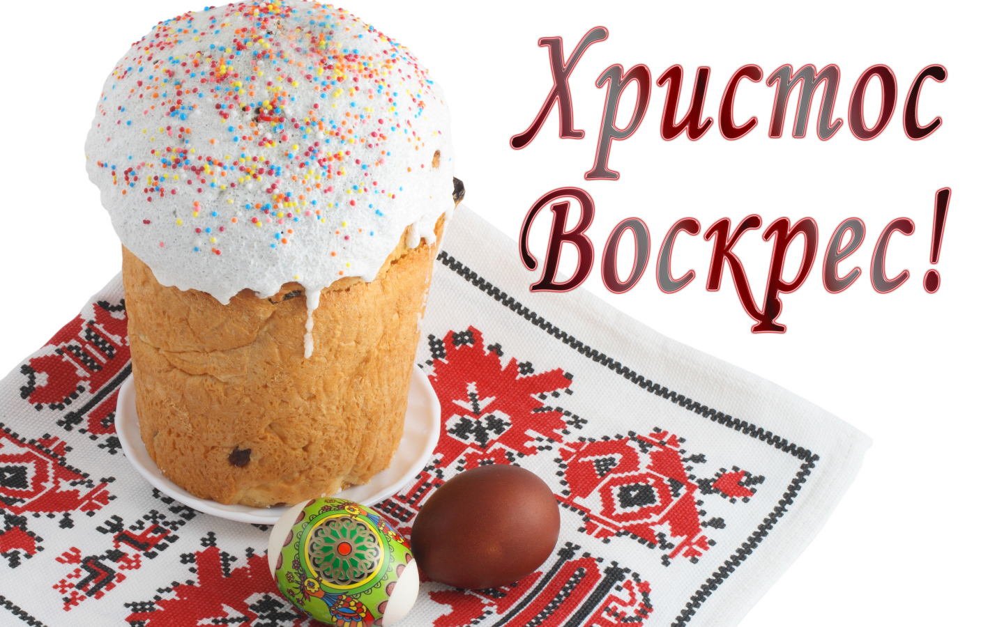Пасхальный кулич с белой глазурью и крашеными яйцами на рушнике с надписью Христос Воскрес на белом фоне