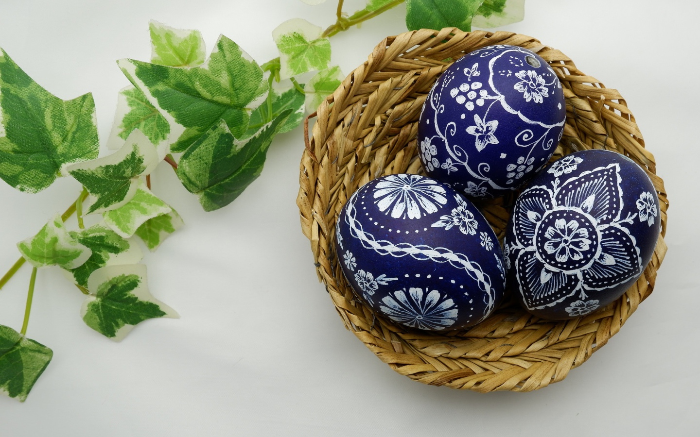 Три раскрашенных яйца в корзинке на столе с веткой 