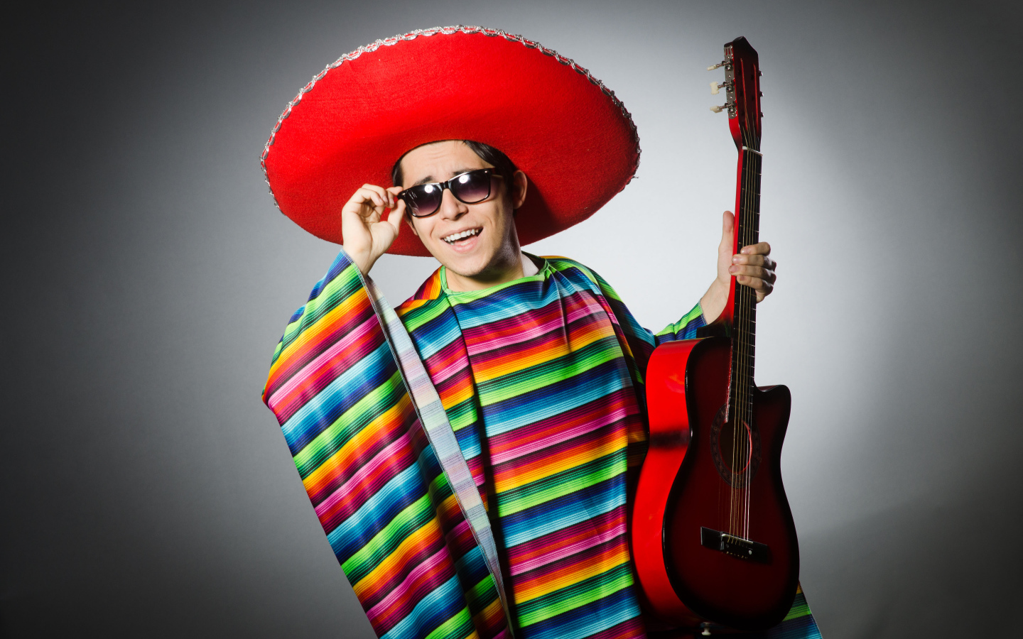 Мужчина в красном сомбреро с гитарой в руках на сером фоне