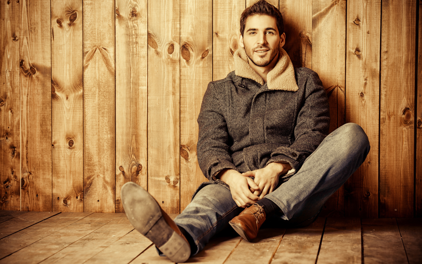 Молодой мужчина в пальто сидит у стены