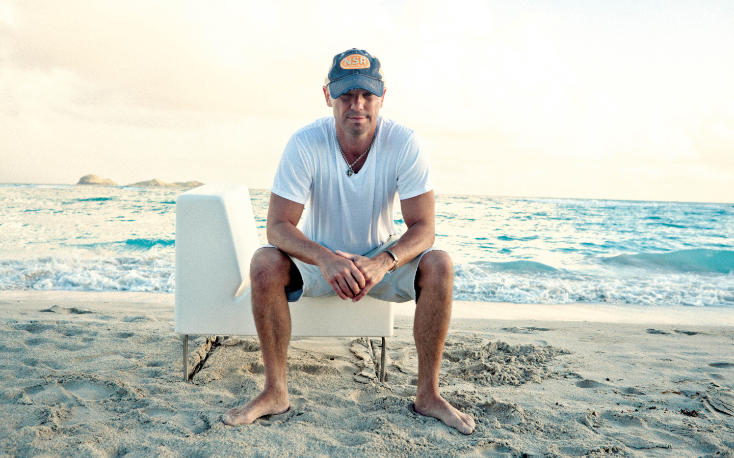 Исполнитель кантри Кенни Чесни на белом кресле на пляже