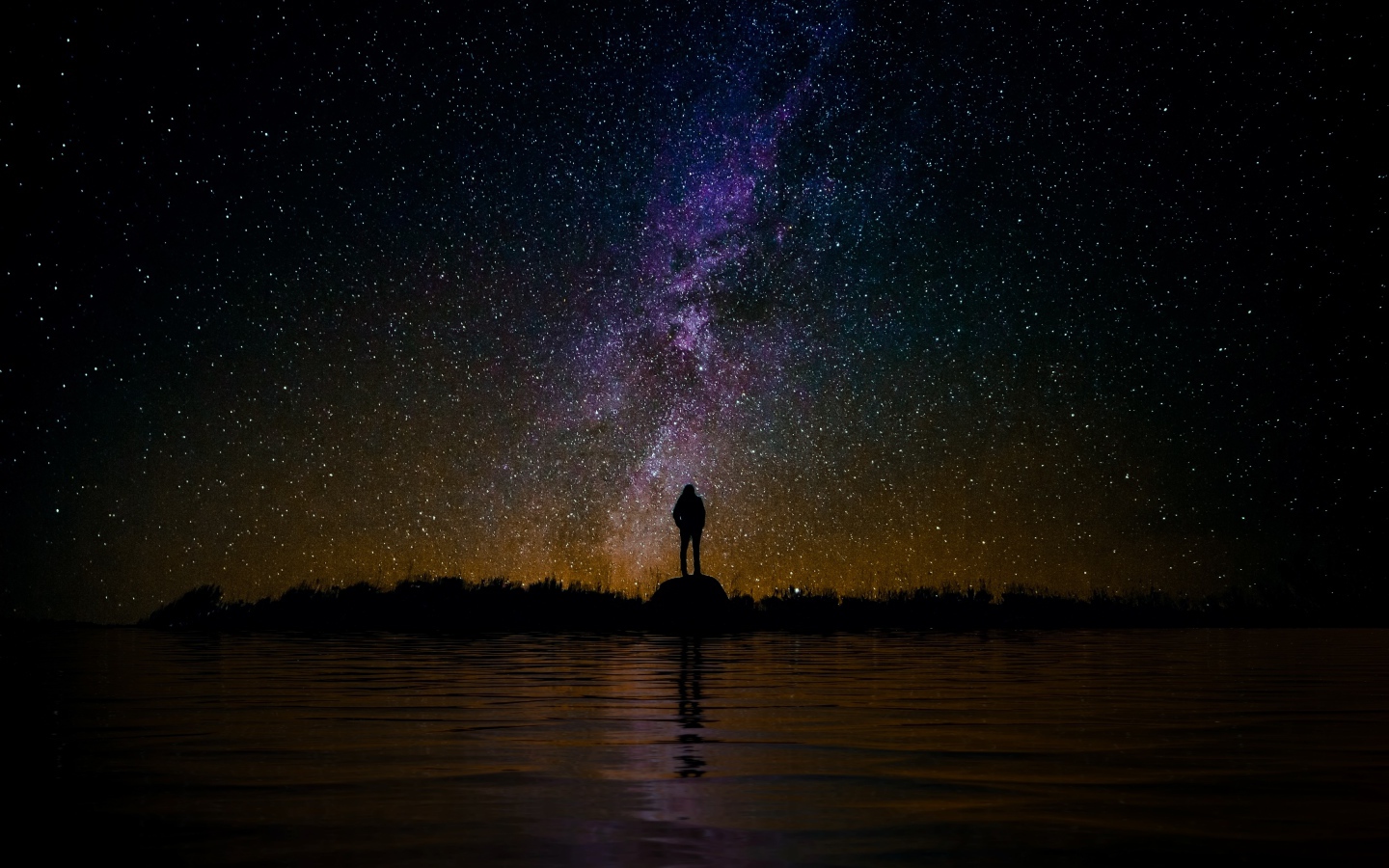 Силуэт человека стоит на камне у воды под звездным небом