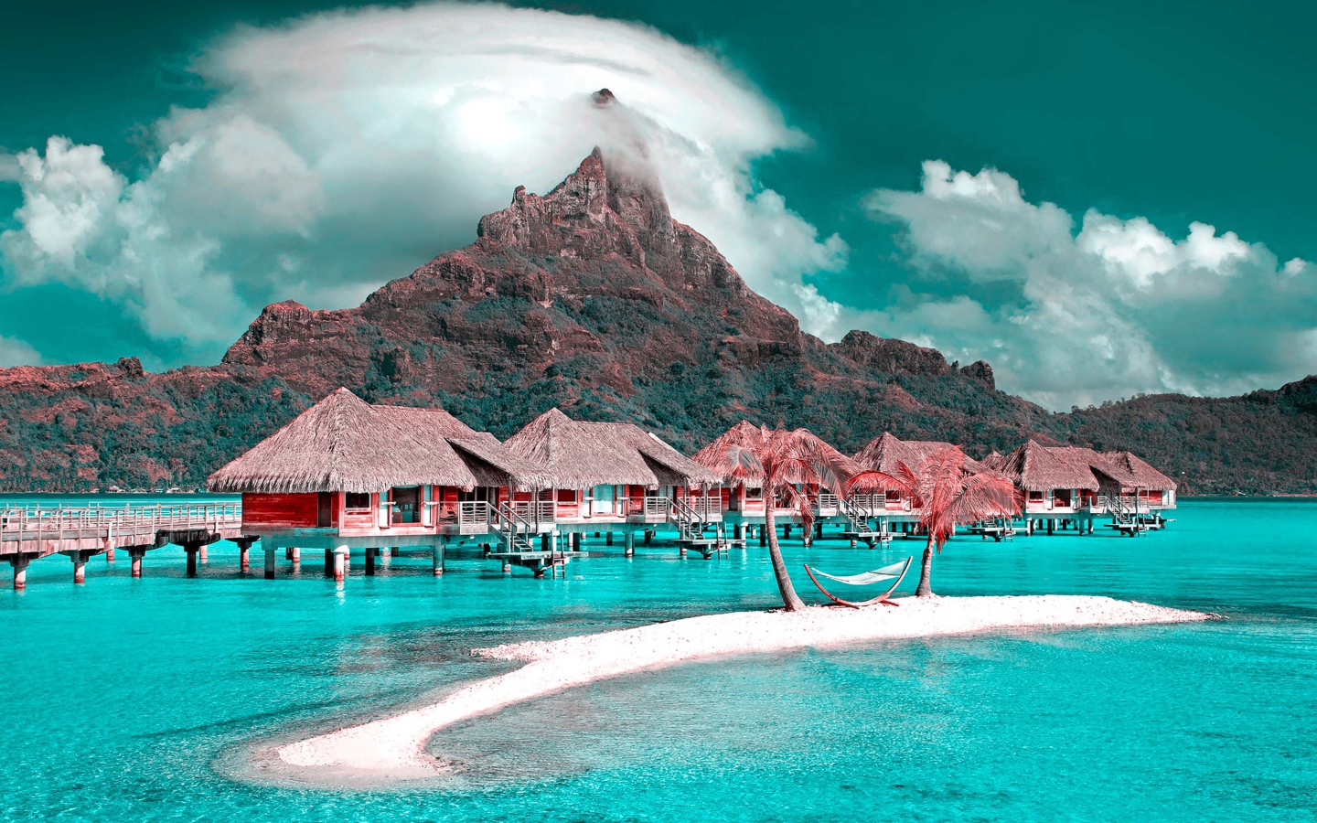 Дома на сваях в голубом океане на фоне горы под белыми облаками