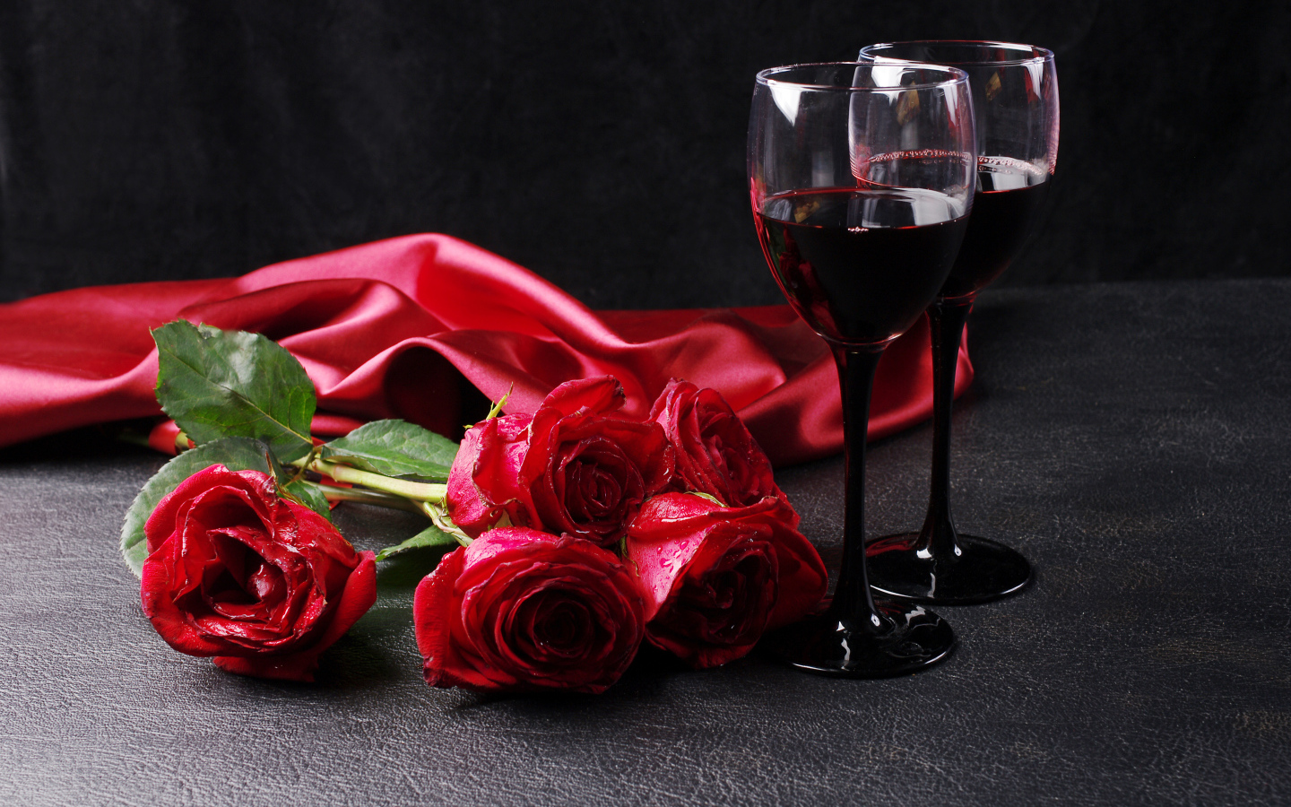 Два бокала с красным вином на черном фоне с букетом красных роз