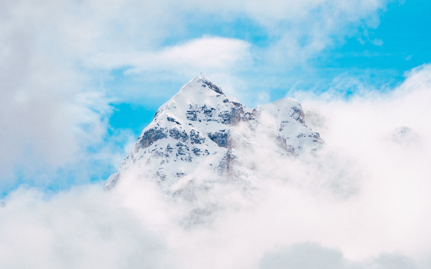 Snow-capped mountain peak in white clouds under blue sky