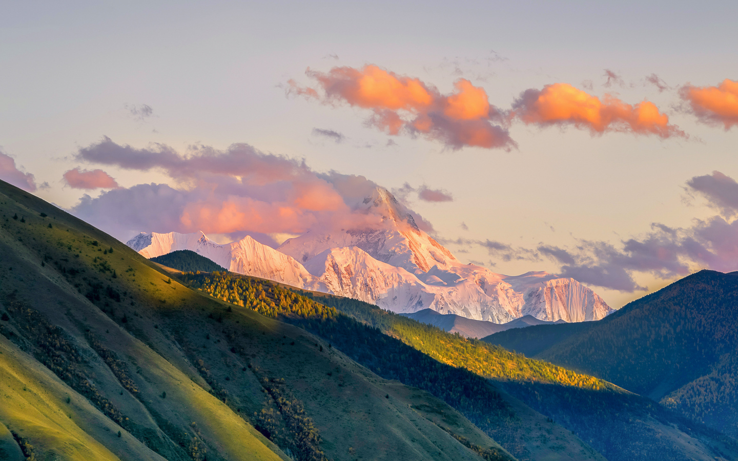 Заснеженные вершины гор у зеленых холмов под голубым небом