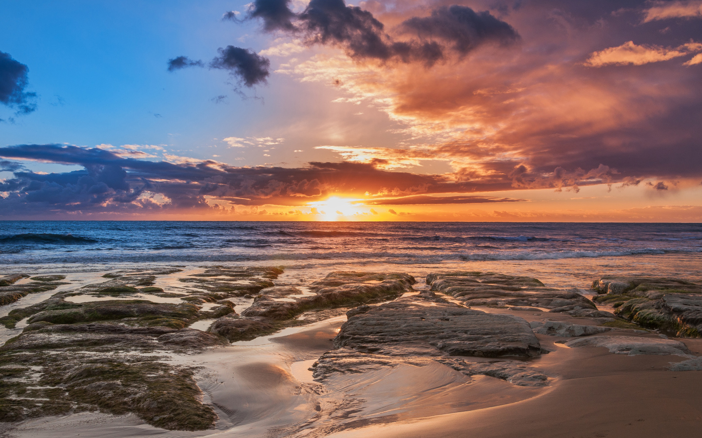 Мокрый песок и камни на берегу океана на закате солнца