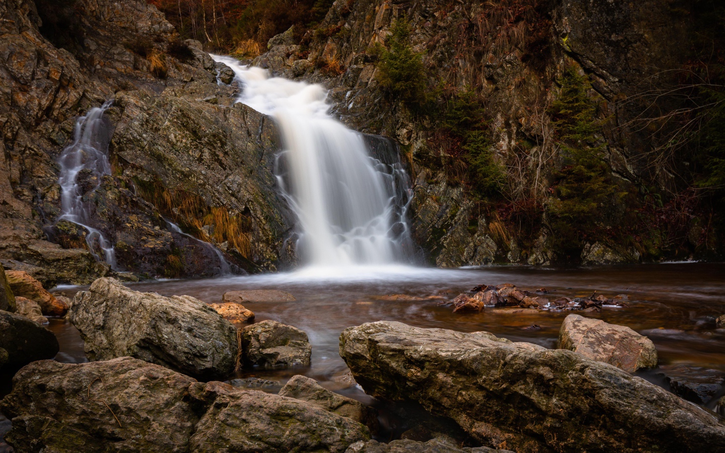 Быстрая вода водопада стекает по камням в горную реку