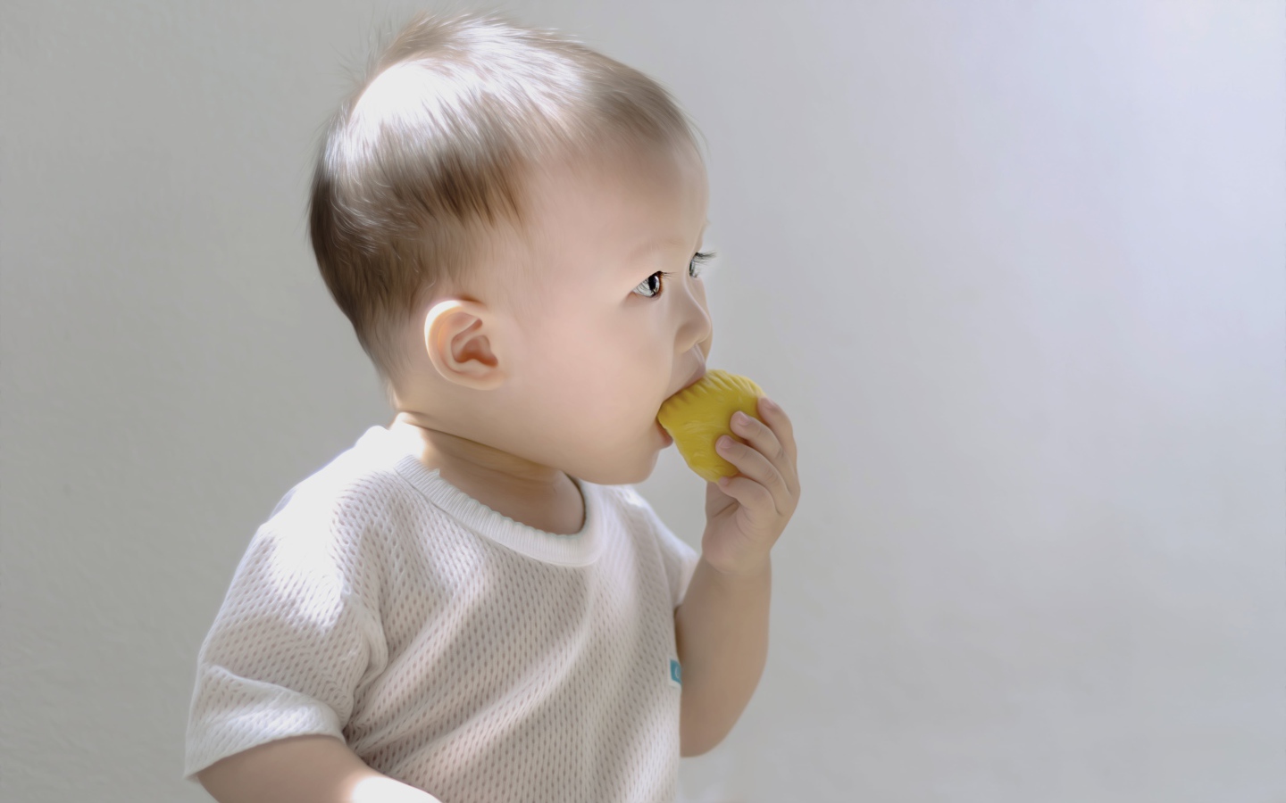Маленький ребенок грызет игрушку на сером фоне