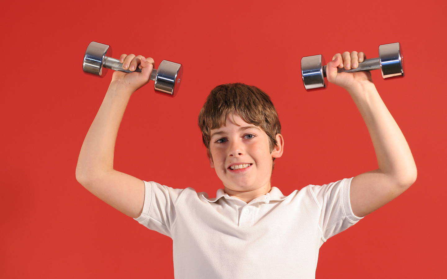 Маленький мальчик с гантелями на красном фоне