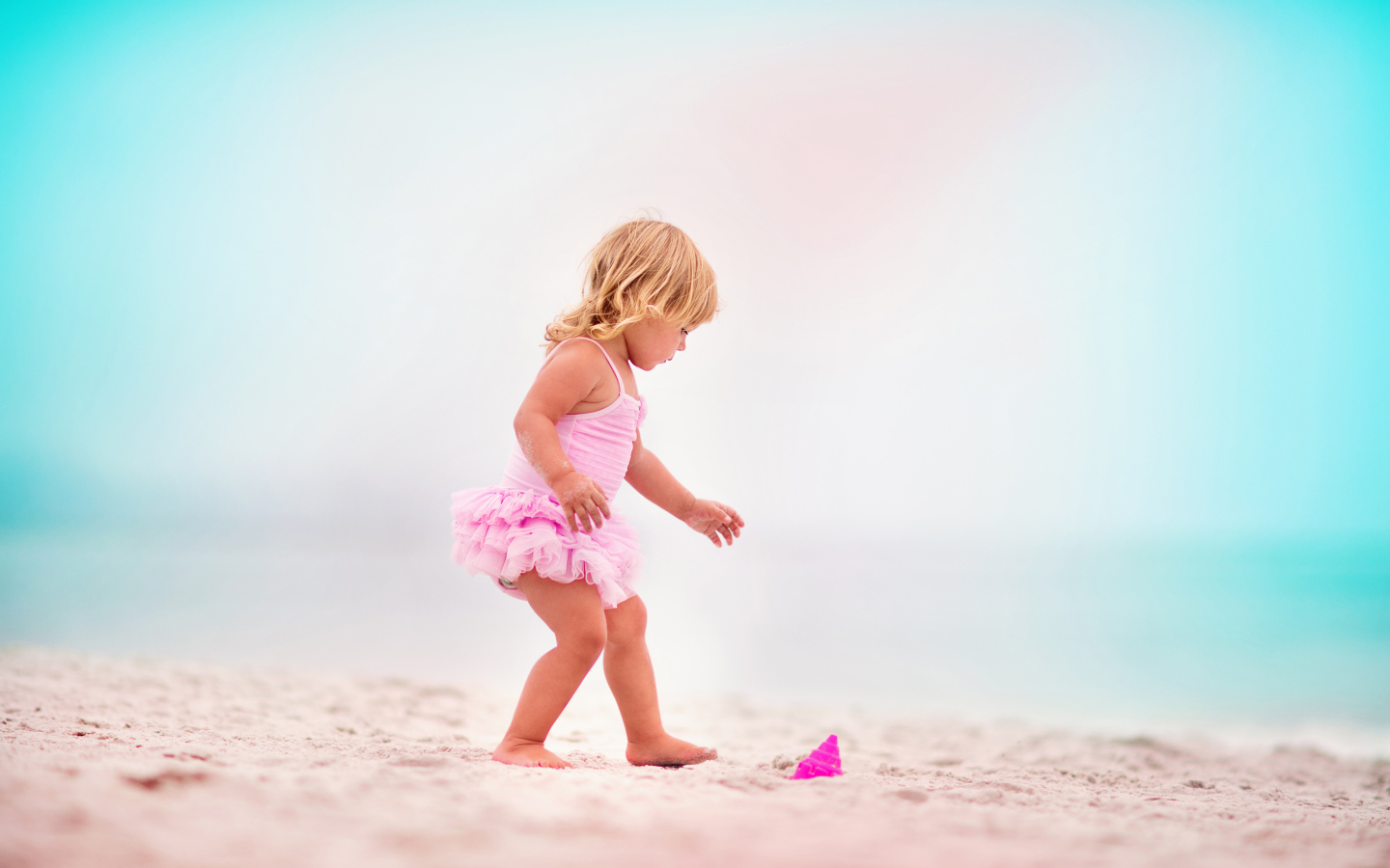 Маленькая девочка в розовом купальнике на песке