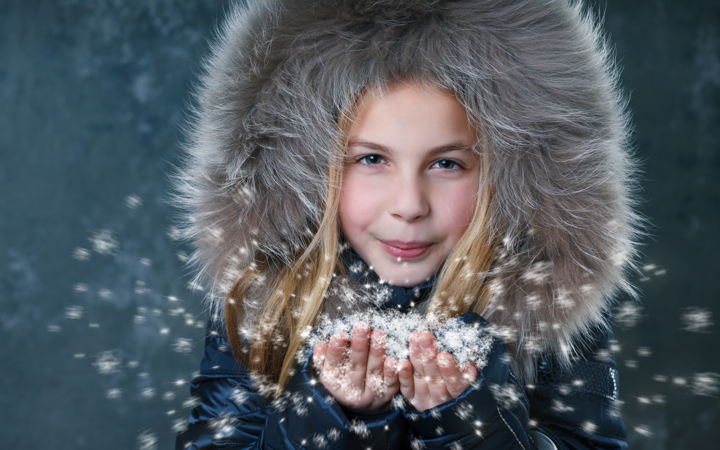 Маленькая девочка в капюшоне сдувает снежинки с ладоней