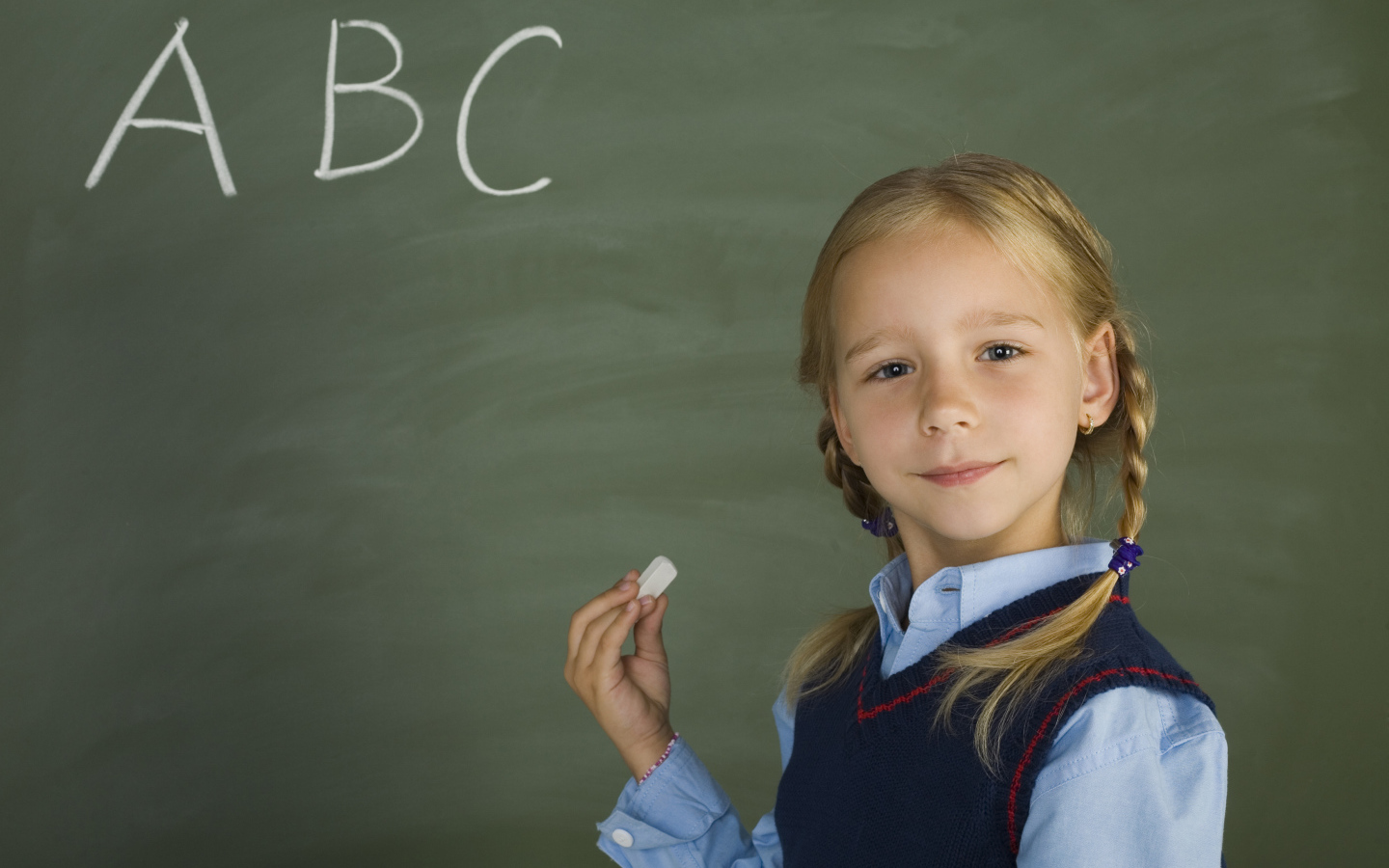 Маленькая школьница пишет буквы на доске 
