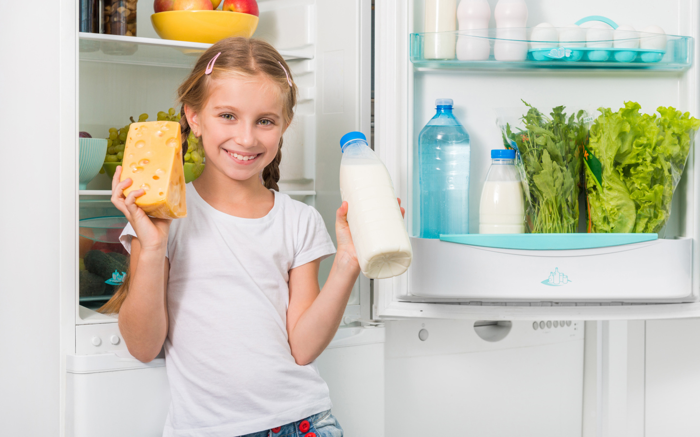 Улыбающаяся девочка у холодильника с сыром и молоком
