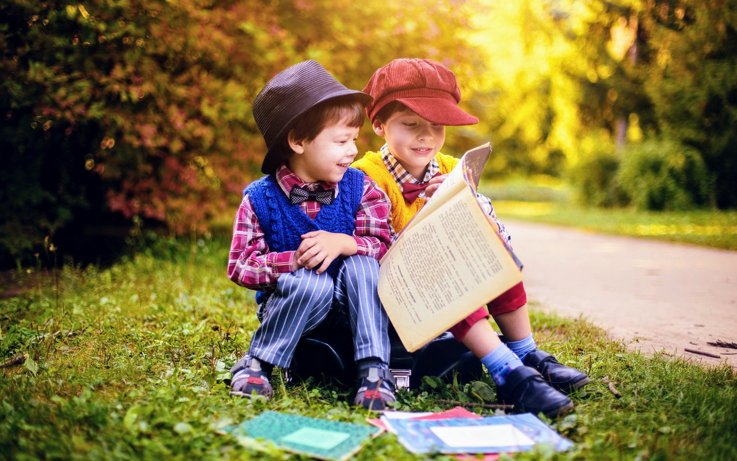 Два маленьких мальчика читают книгу сидя на траве