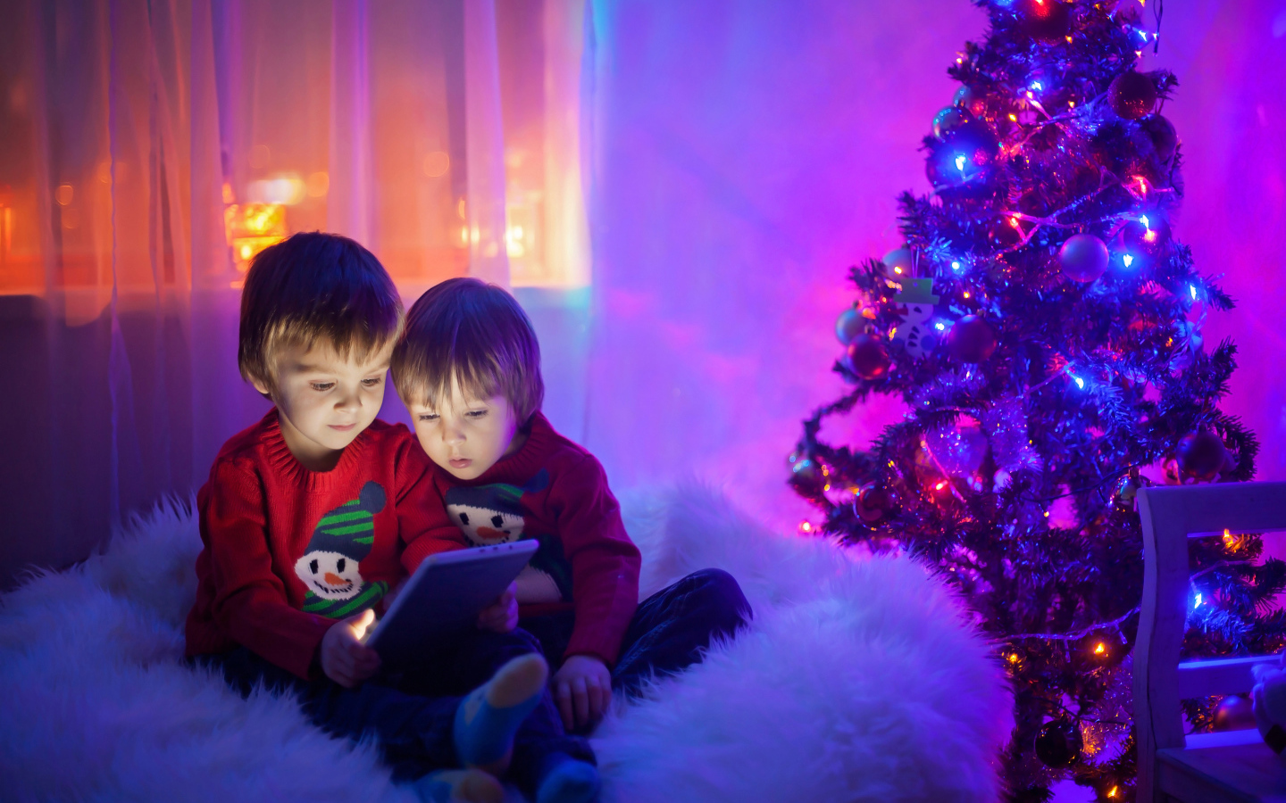 Two little boys watching cartoons by the New Year tree