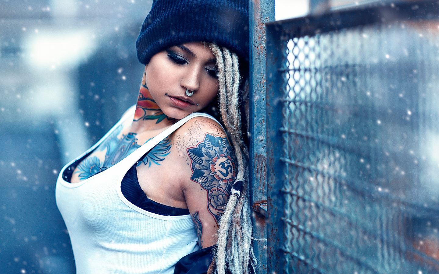 Девушка с татуировками на шее и пирсингом в носу у забора