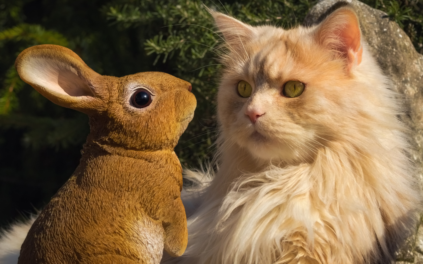 Пушистый рыжий кот сидит в парке со статуэткой кролика 