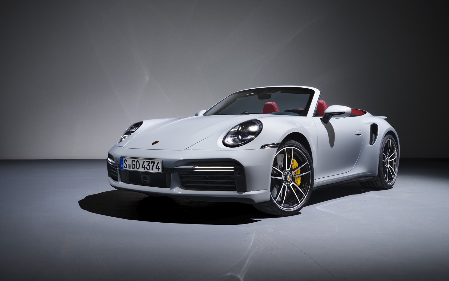 Белый кабриолет Porsche 911 Turbo S 2020 года на сером фоне
