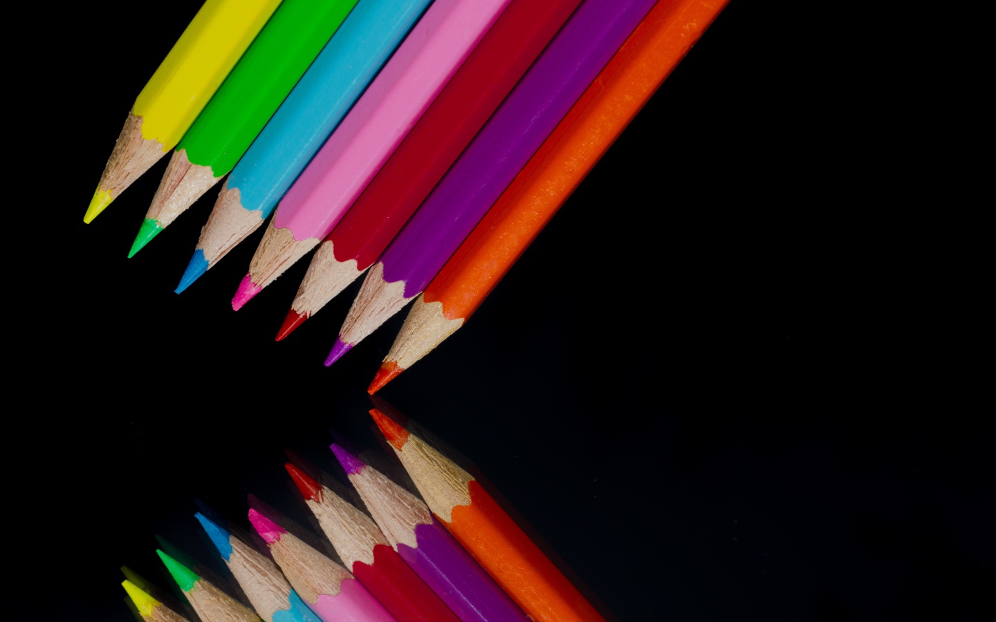 Разноцветные карандаши отражаются в черной зеркальной поверхности 