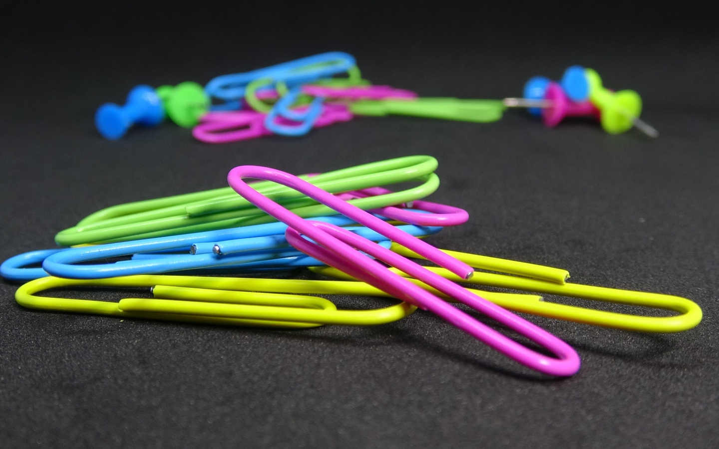 Разноцветные скрепки на черном столе 