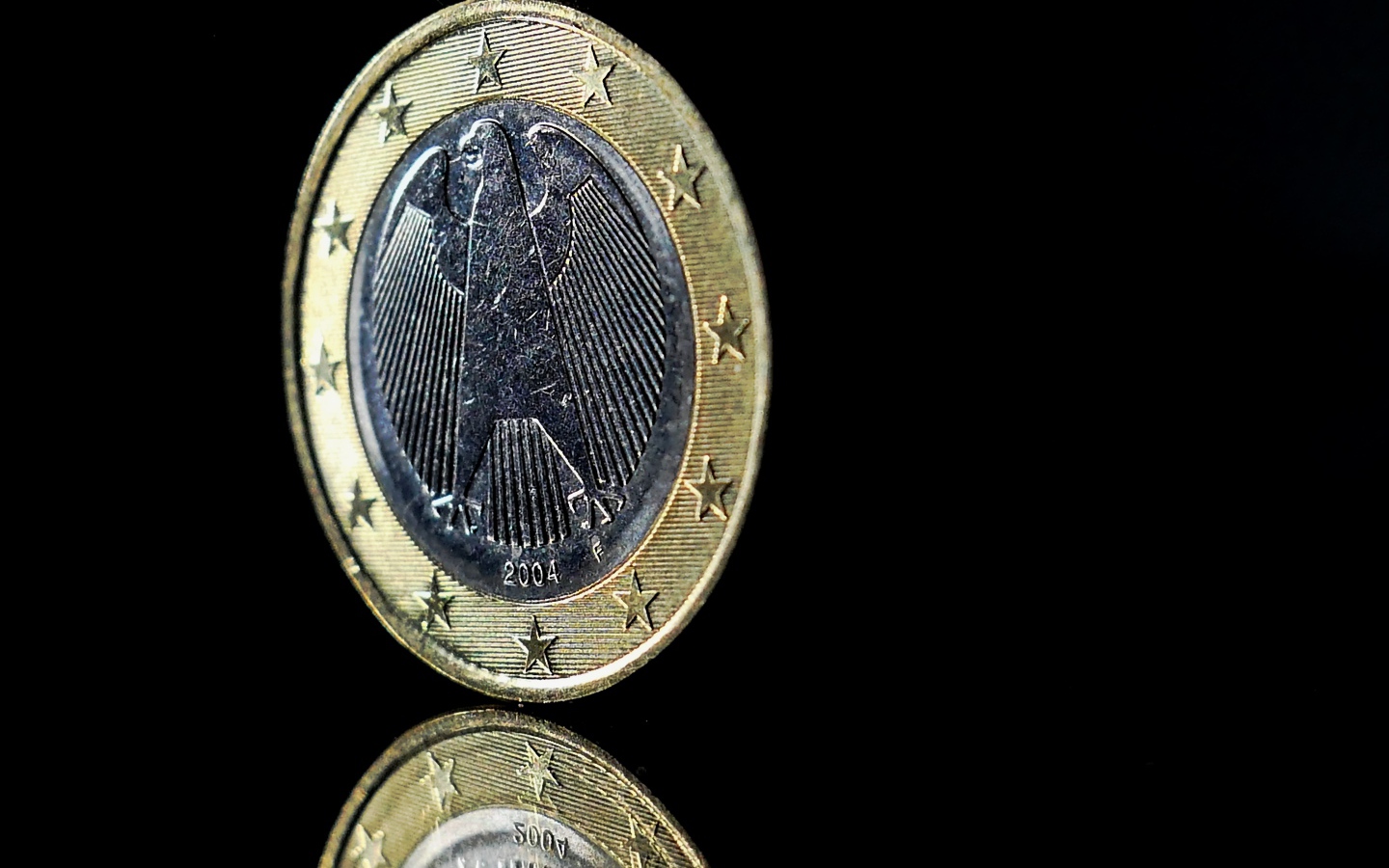 Монета евро стоит на ребре на черном фоне 
