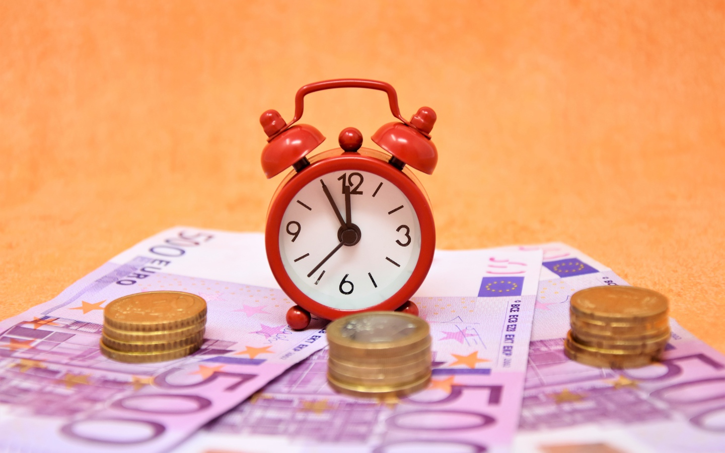 Маленький красный будильник с купюрами евро и монетами