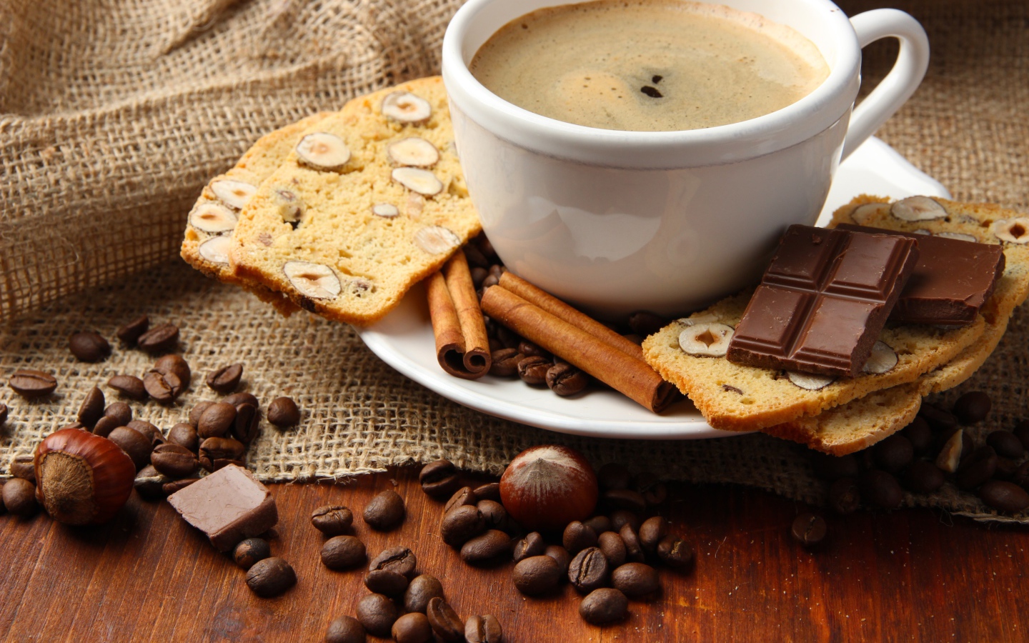 Чашка кофе на тарелке с кексом, шоколадом, корицей и зернами 