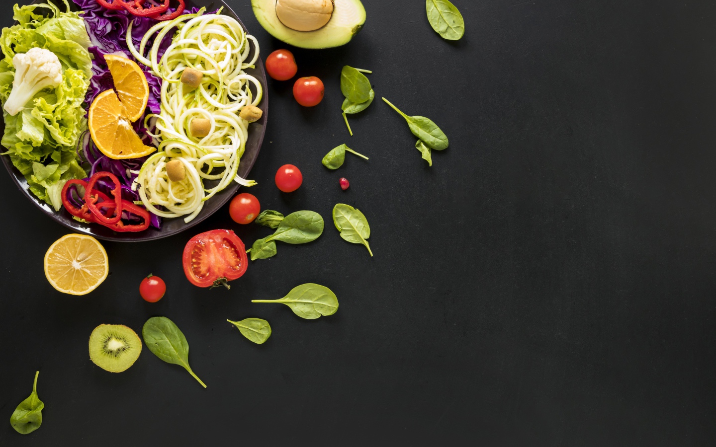 Салат из свежих овощей на черном столе с базиликом, помидорами и авокадо 