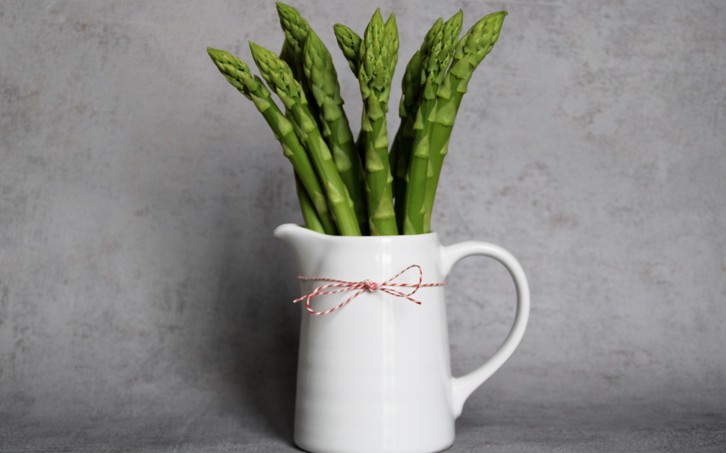 Зеленая спаржа в белой вазе на фоне серой стены