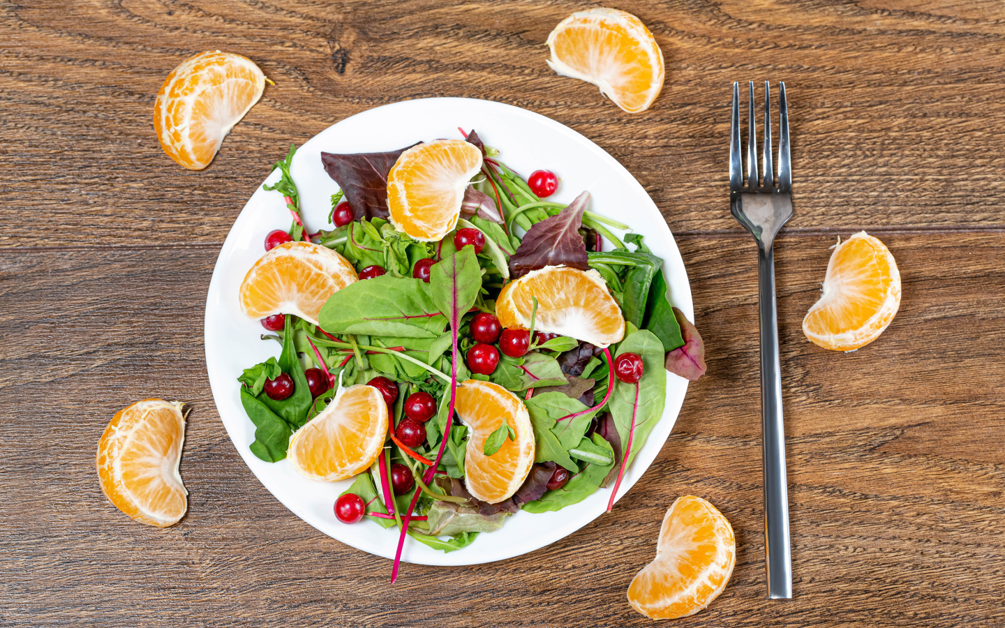 Салат из зелени и мандарина на белой тарелке на столе с вилкой