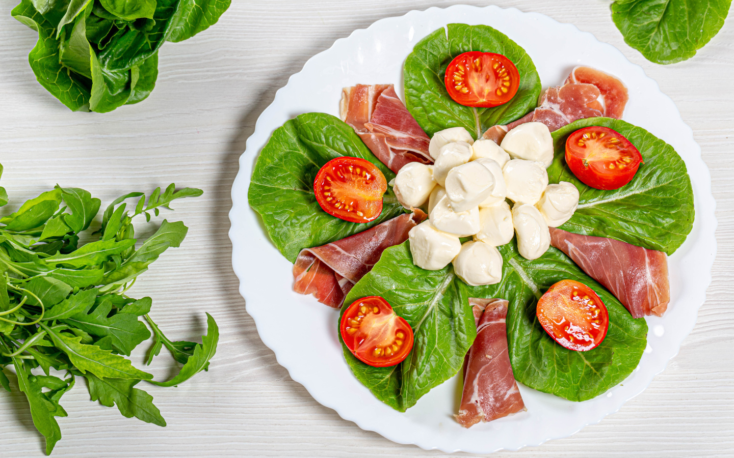 Кусочки ветчины на тарелке с сыром, помидорами и листьями салата