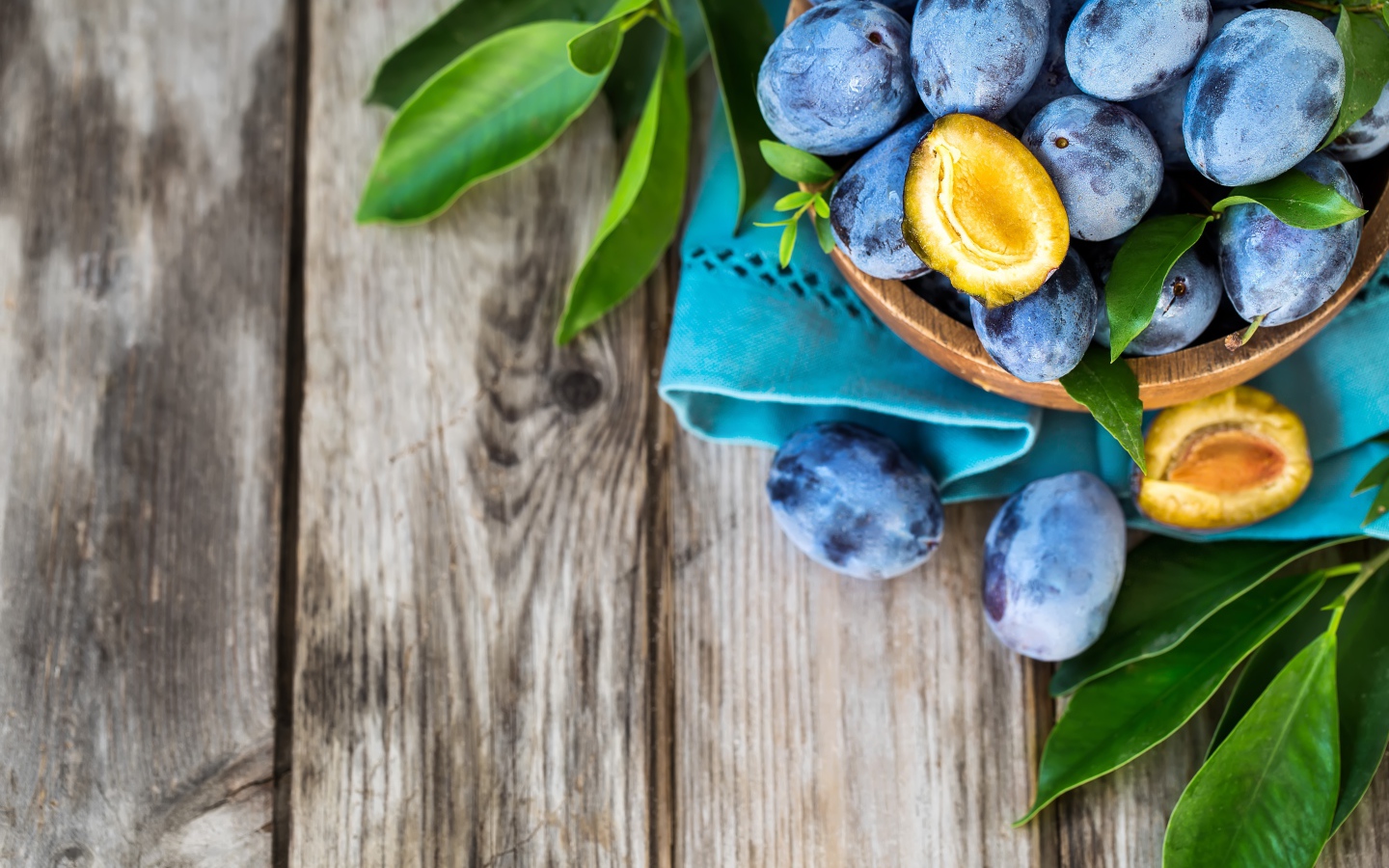 Свежие синие сливы с зелеными листьями на столе 