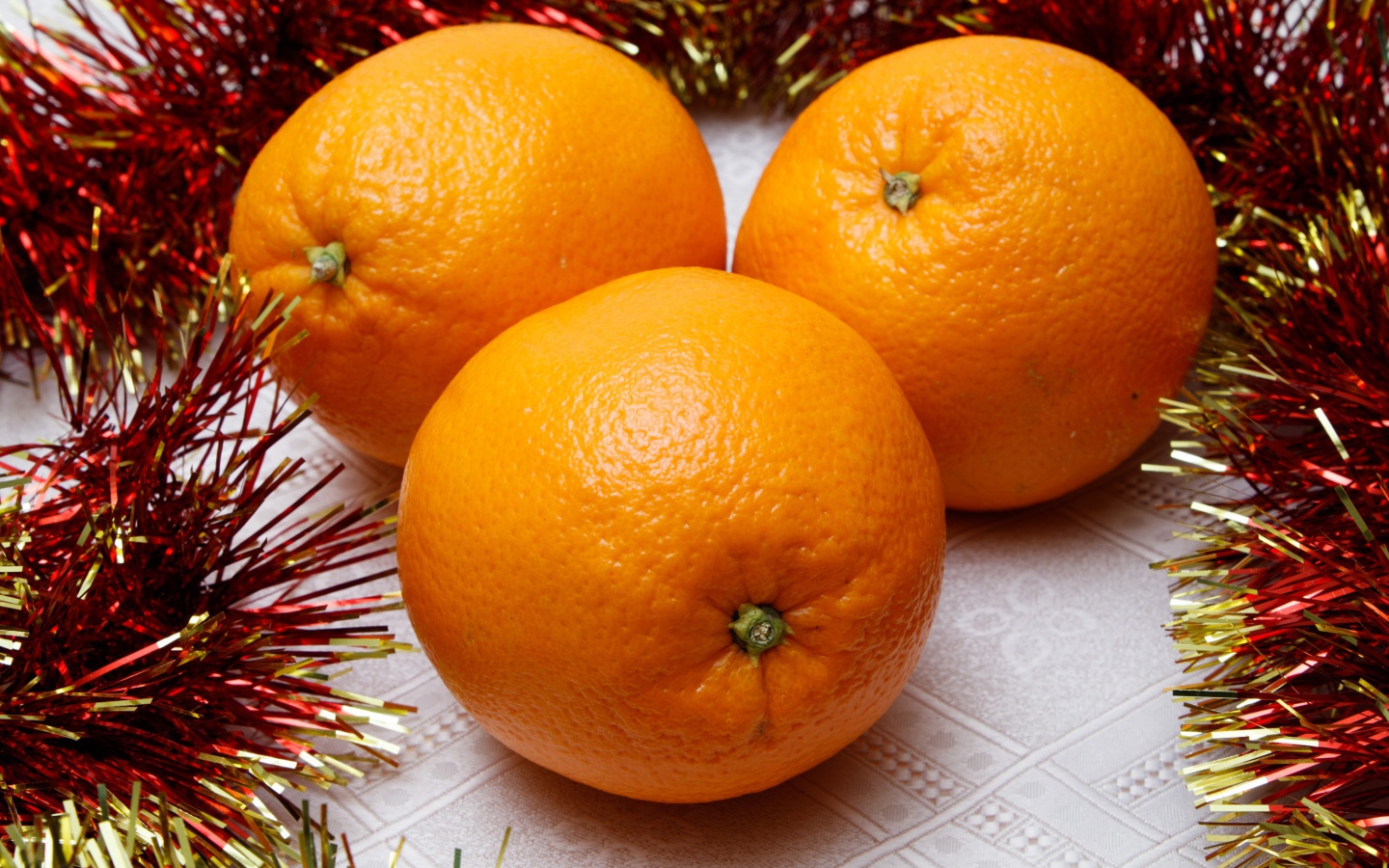 Three large oranges on the table with tinsel