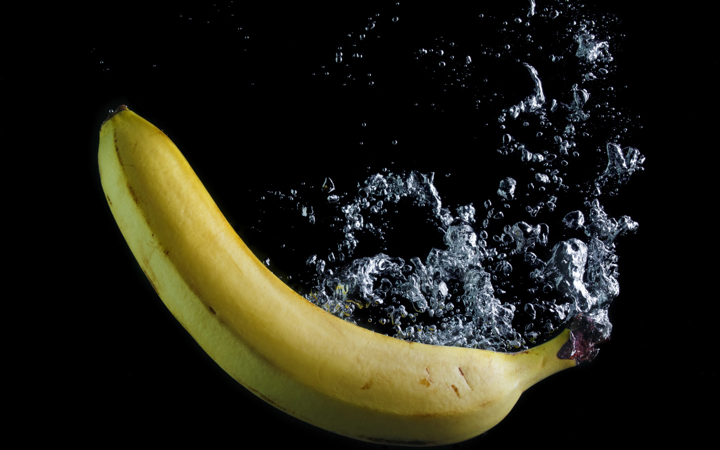 Желтый банан в воде на черном фоне