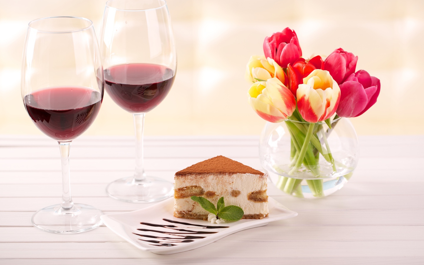 Кусок  тирамису на столе с бокалами вина и букетом тюльпанов