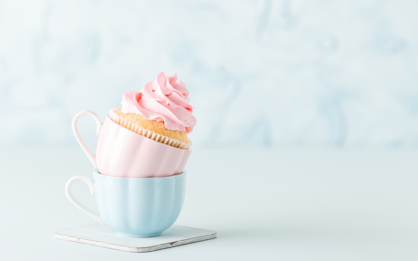 Кекс с розовым кремом с чашками на столе 