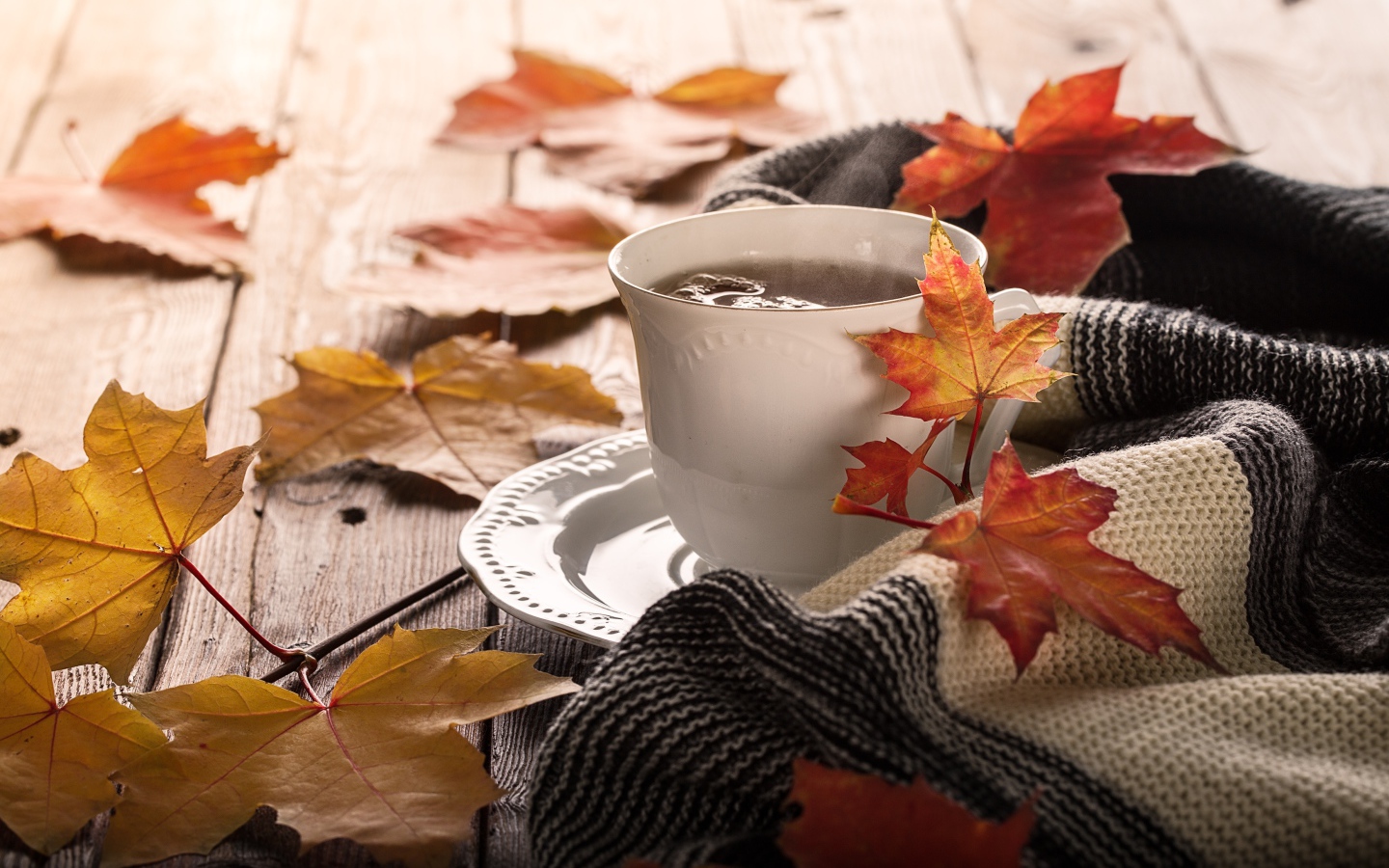 Чашка чая на столе с осенними листьями и пледом