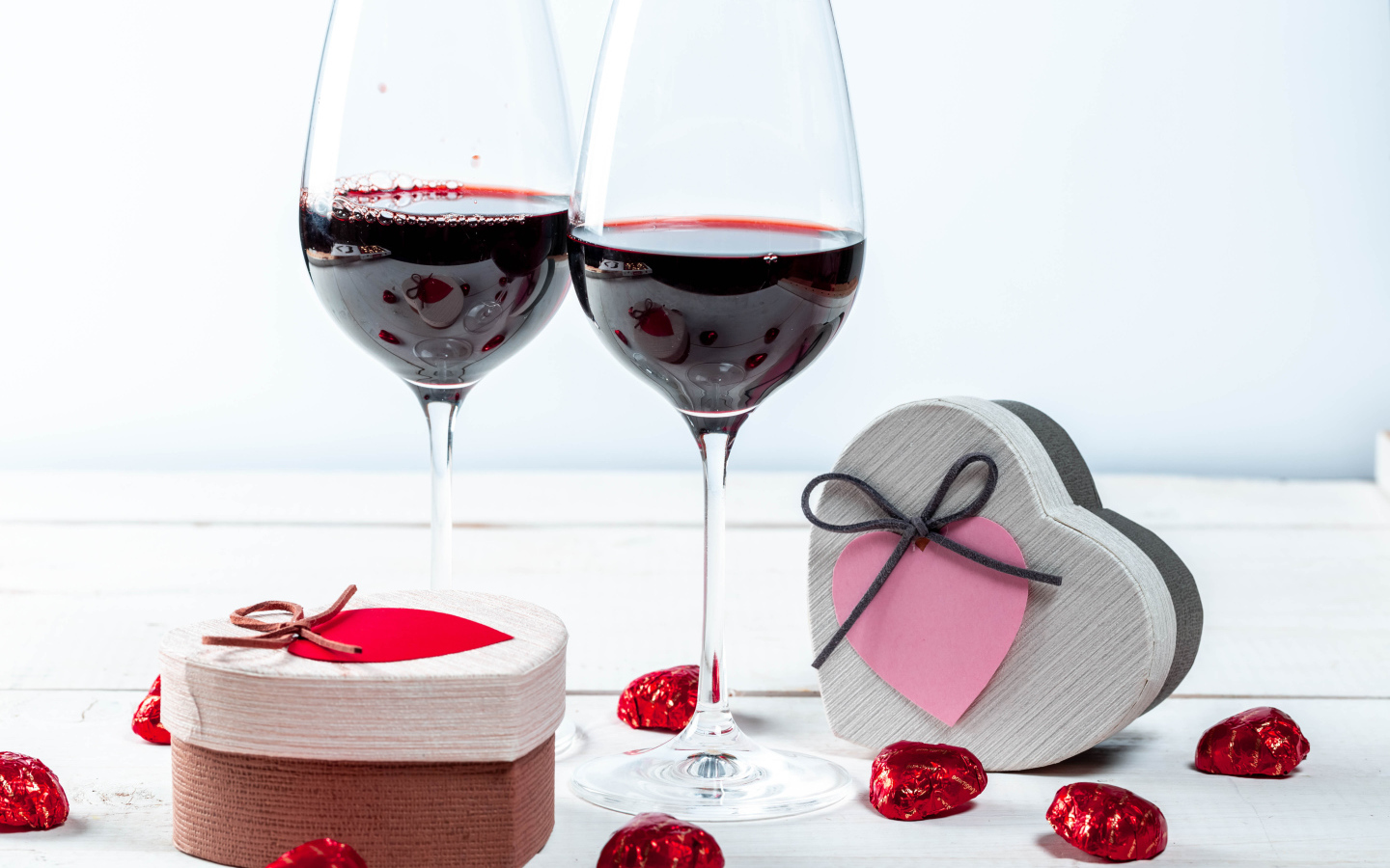 Две коробки с конфетами в форме сердца на столе с бокалами 