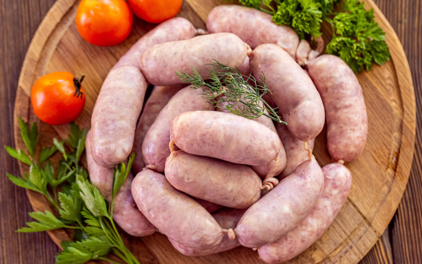 Свежие сырые домашние сардельки на доске с петрушкой и помидорами