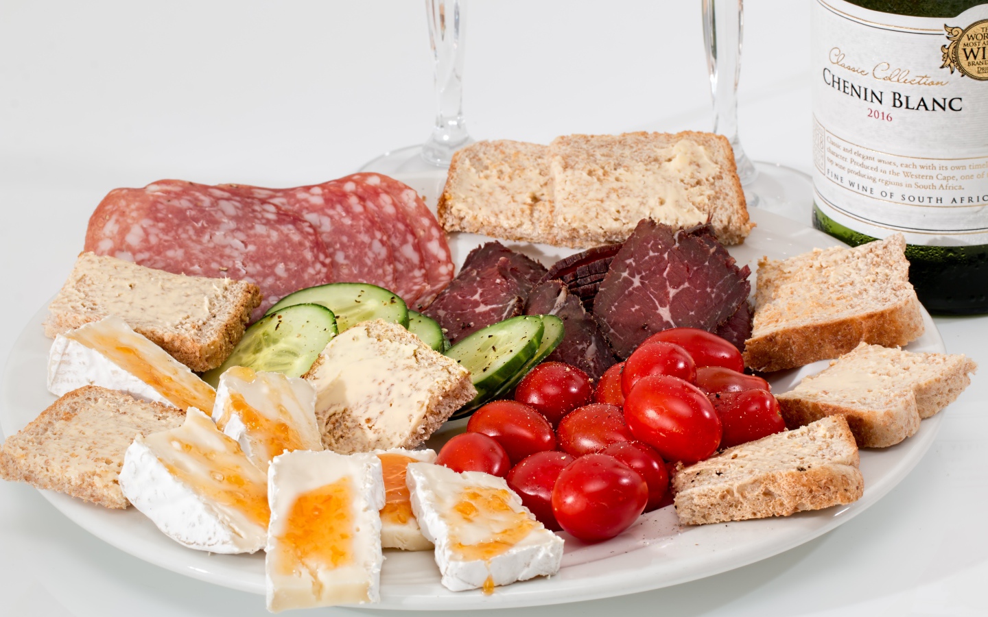 Тарелка с мясными продуктами, яйцами, овощами и хлебом на столе с вином