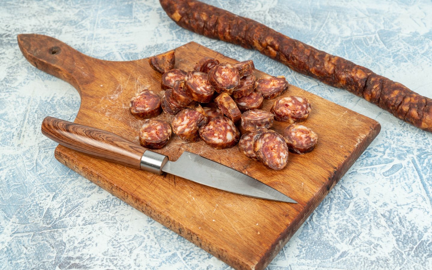 Колбаса нарезана колечками на разделочной доске с ножом 