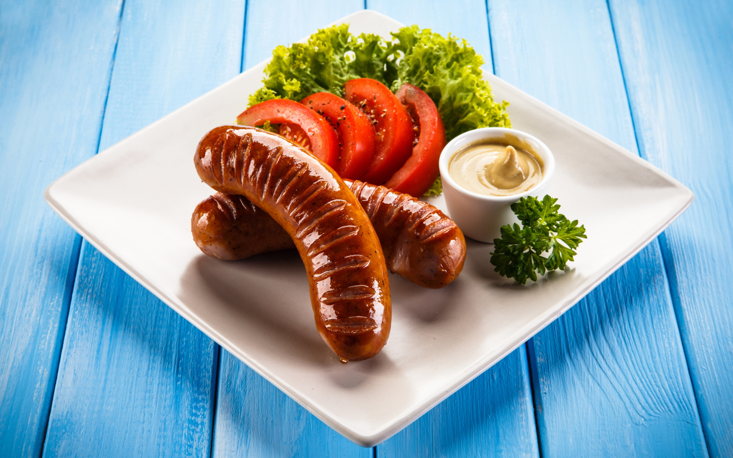 Две жареные колбаски на тарелке с помидорами, горчицей и листьями салата 