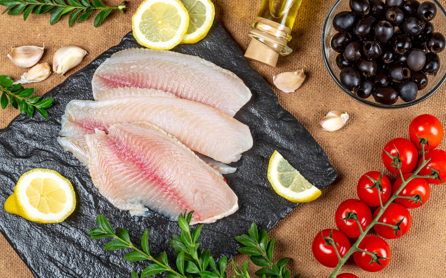 Филе рыбы на столе с лимоном, помидорами и оливками