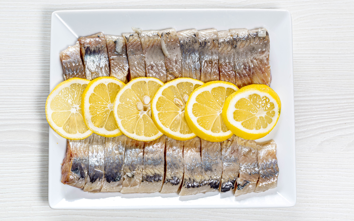 Селедка нарезанная кусочками на белой тарелке с лимоном 