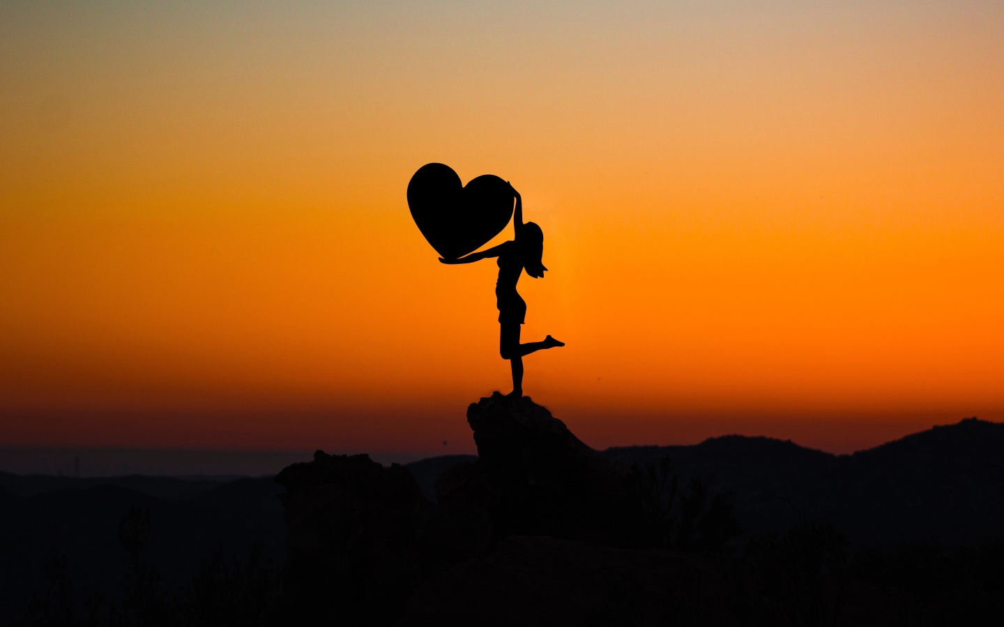 Silhouette girl with a heart in hands on a sunset background