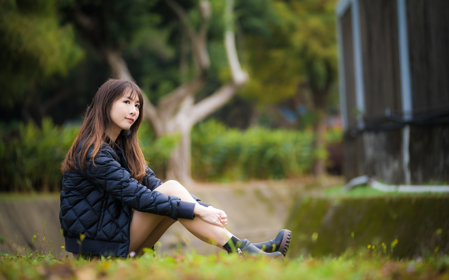 Девушка азиатка в черной куртке сидит на траве