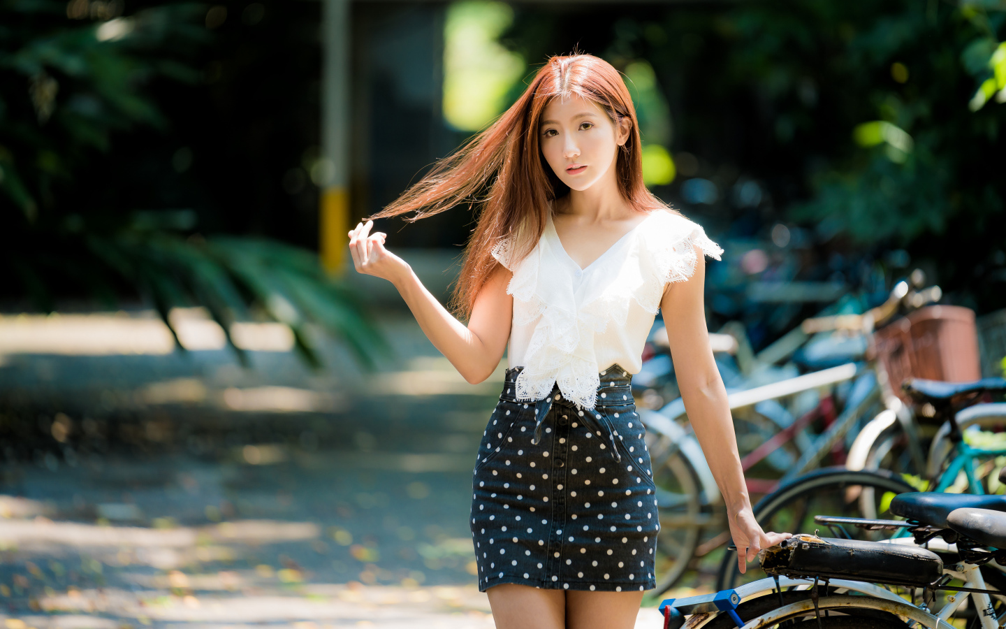 Девушка азиатка в юбке в горох у велосипеда трогает волосы