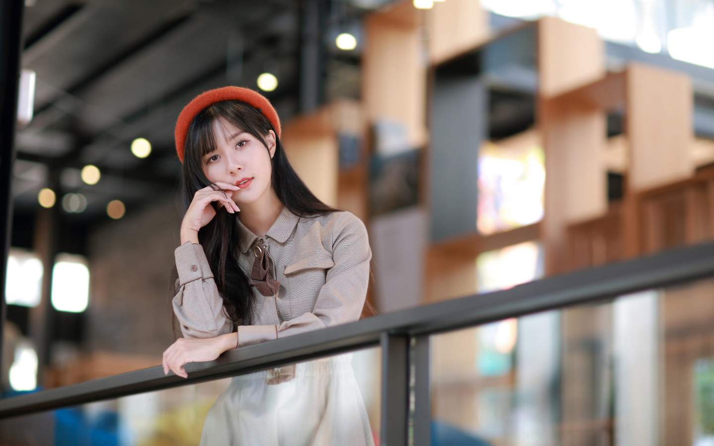 Азиатка в сером платье стоит у перил 