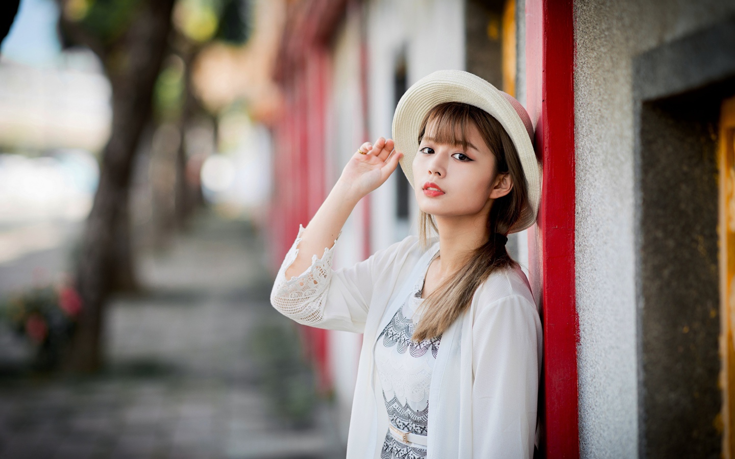 Красивая азиатка в шляпе стоит у стены